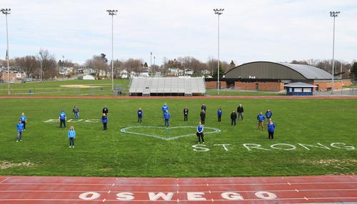 Students on a sports field with a chalk drawing of a heart and the words "Buc Strong Oswego"